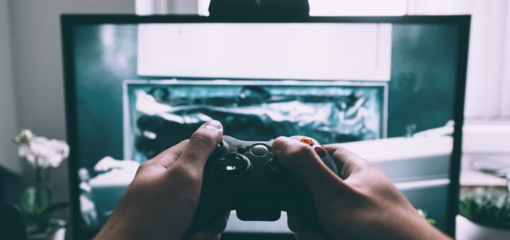 person holding game controller in-front of television